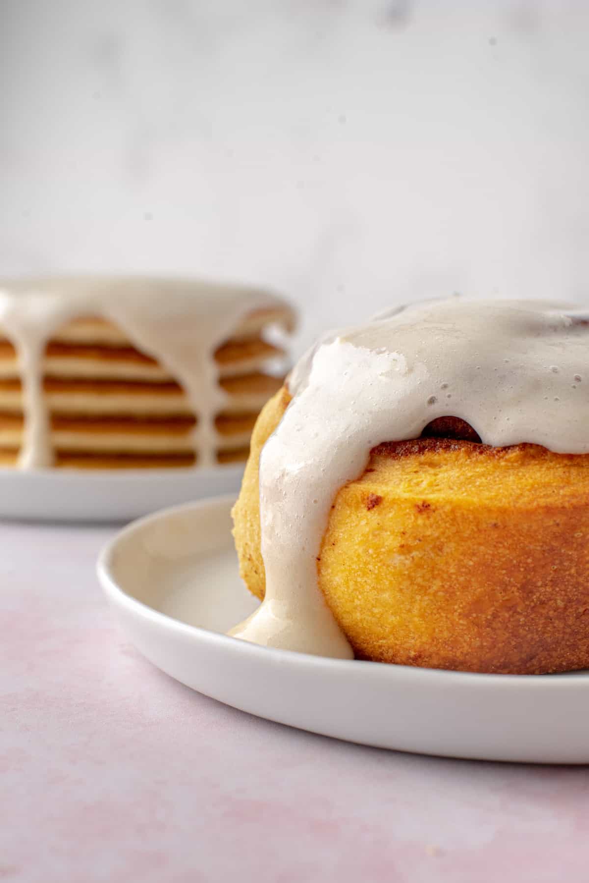 Cream cheese glaze on a cinnamon roll and a stack of pancakes.