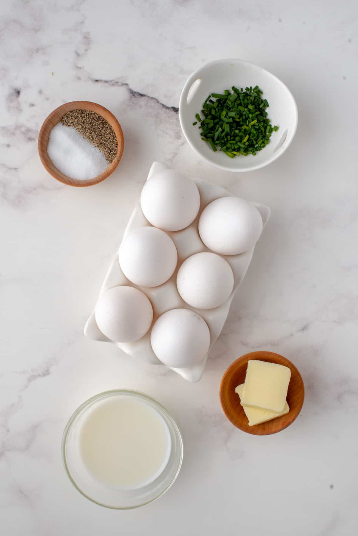 Overhead view of ingredients needed including eggs, butter, chives, milk, salt and pepper.