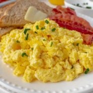Scrambled eggs on a plate with bacon and toast.