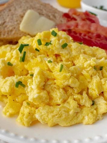 Scrambled eggs on a plate with bacon and toast.