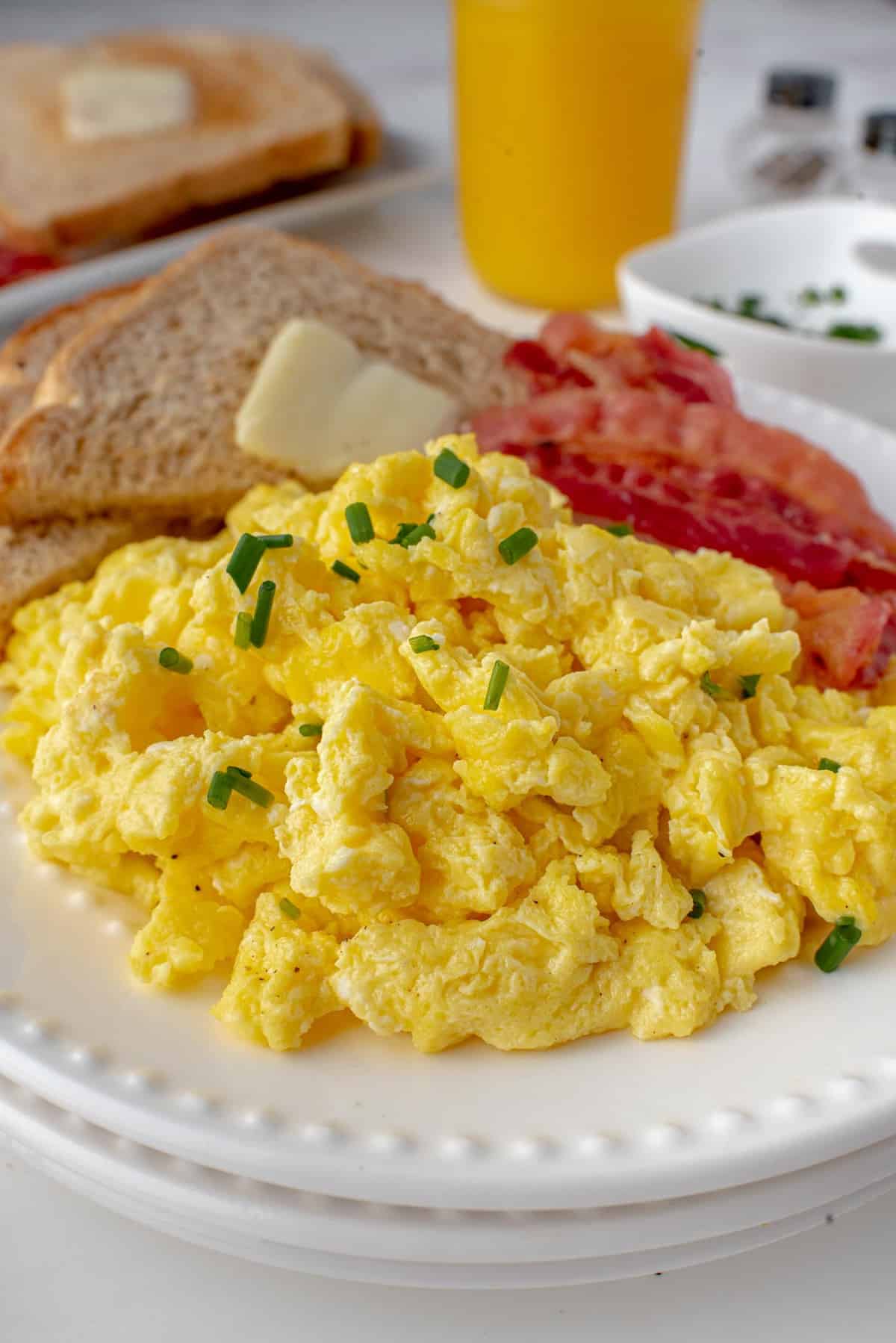 Scrambled eggs piled on a plate with bacon and toast.