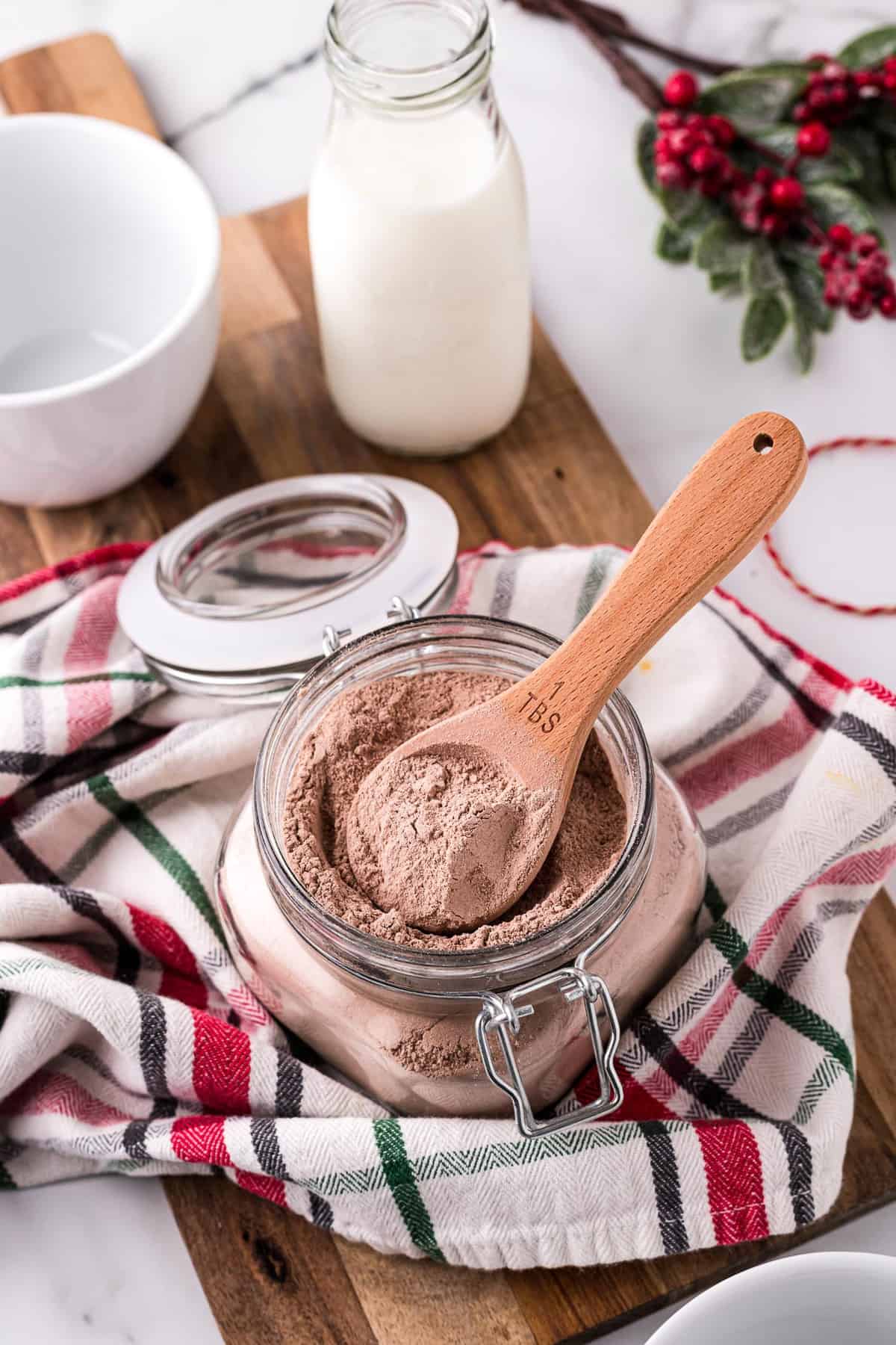 Hot cocoa mix in a small glass jar with a wooden spoon.