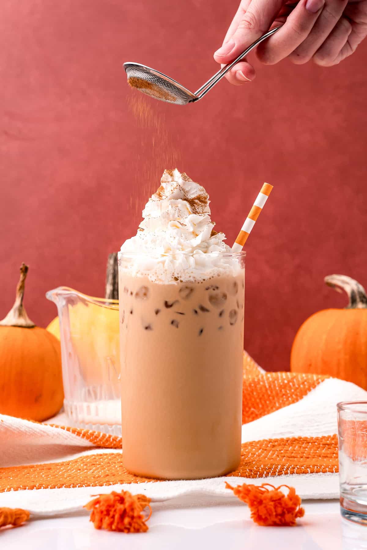 Pumpkin pie spice being sprinkled on an iced latte.