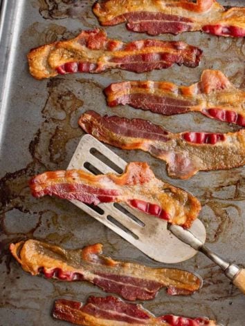 Bacon on a baking sheet, one slice on a spatula.