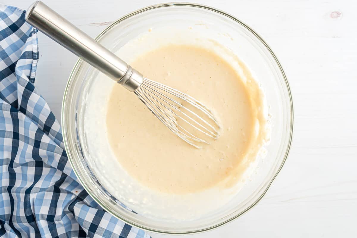 Pancake batter and a whisk in a glass mixing bowl.