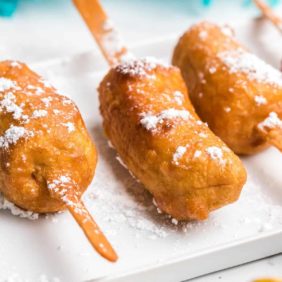 Battered and fried bananas on a stick, sprinkled with powdered sugar.