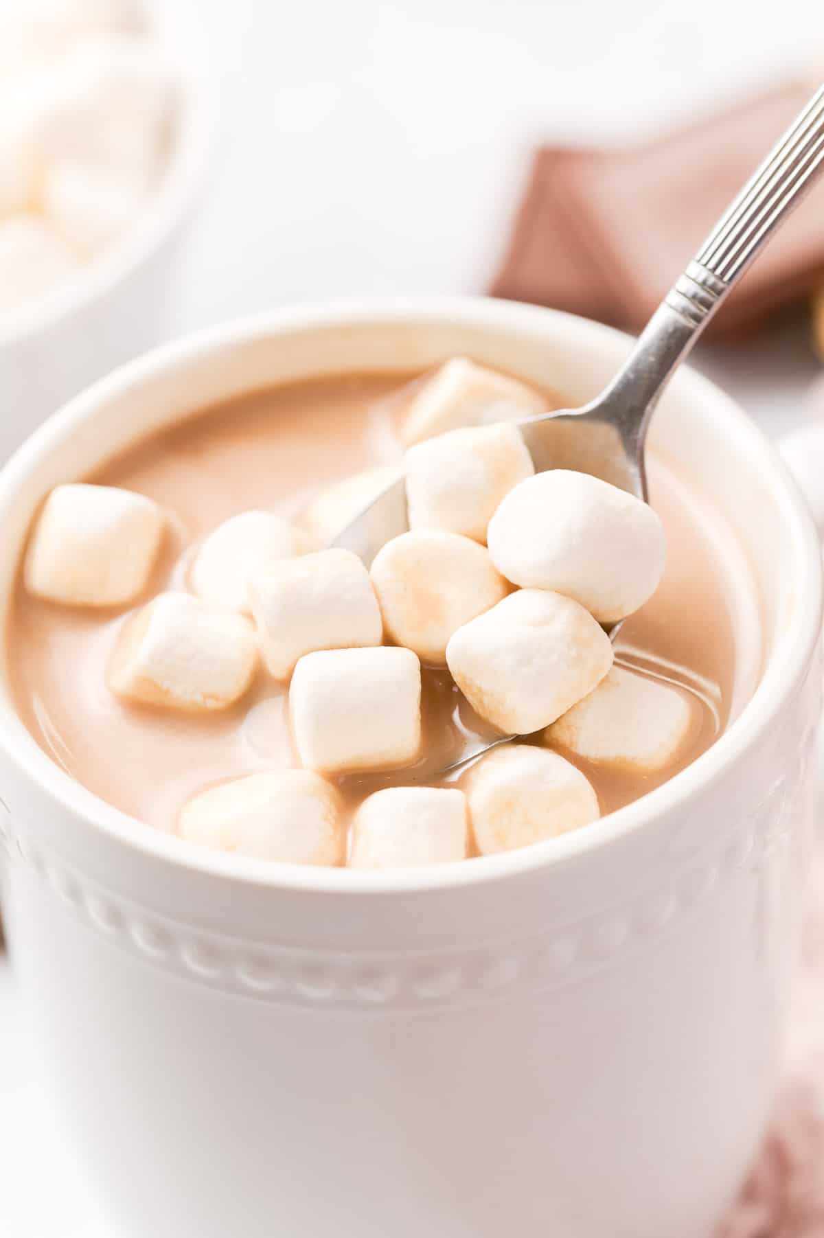 Marshmallows being added to hot cocoa with a spoon.