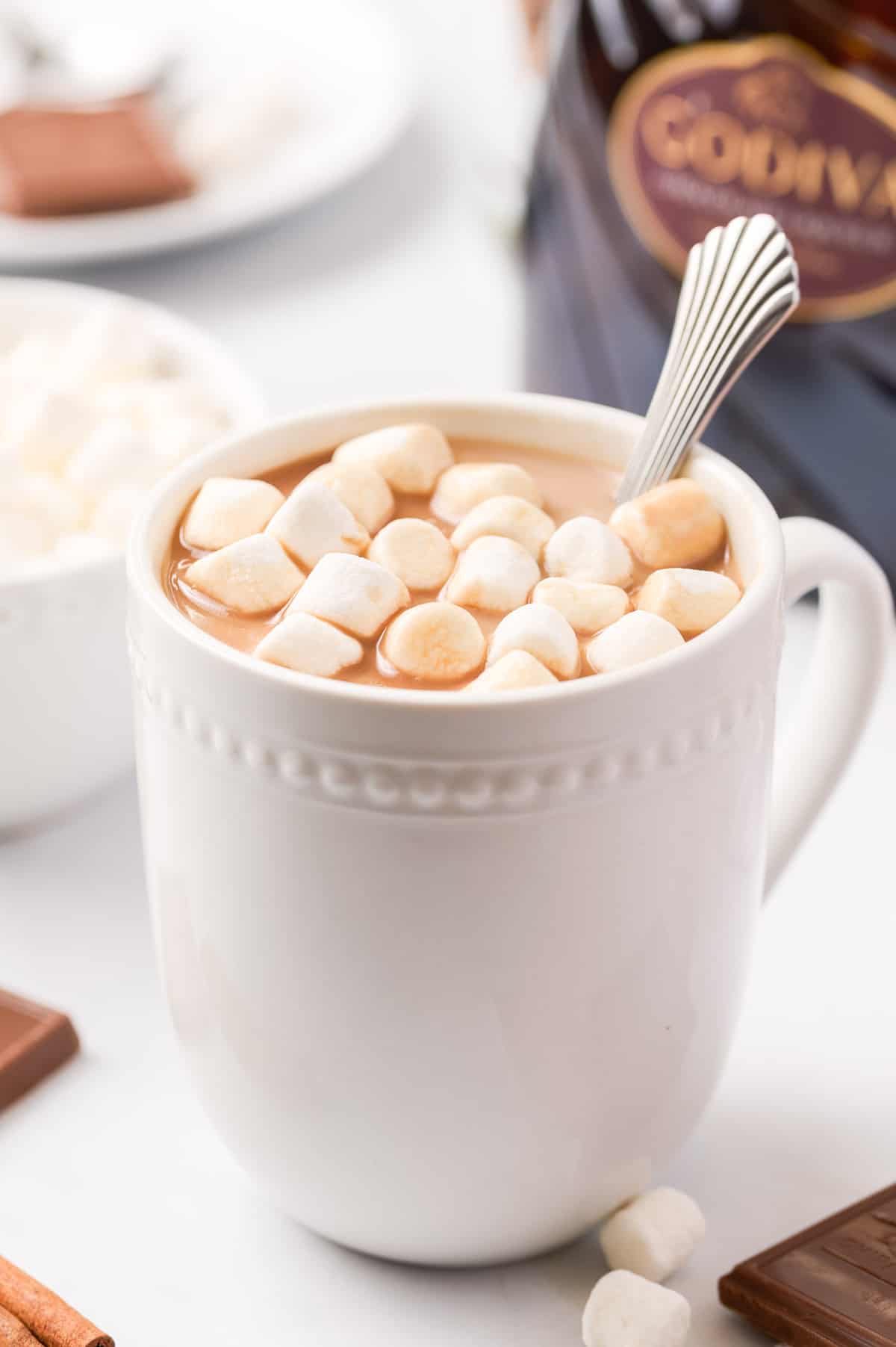 White mug of a cup of spiked hot chocolate with a spoon and marshmallows.