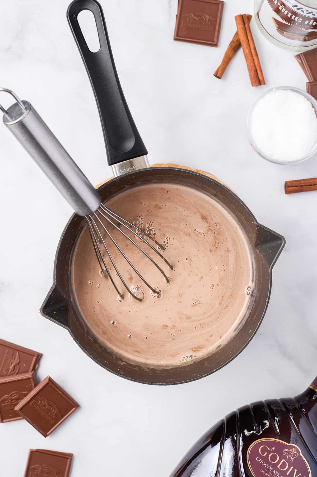 Hot chocolate in a saucepan with a whisk.