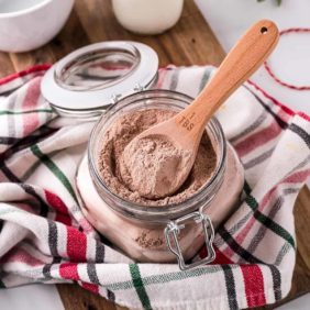 Hot cocoa mix in small glass jar with a little wooden spoon.