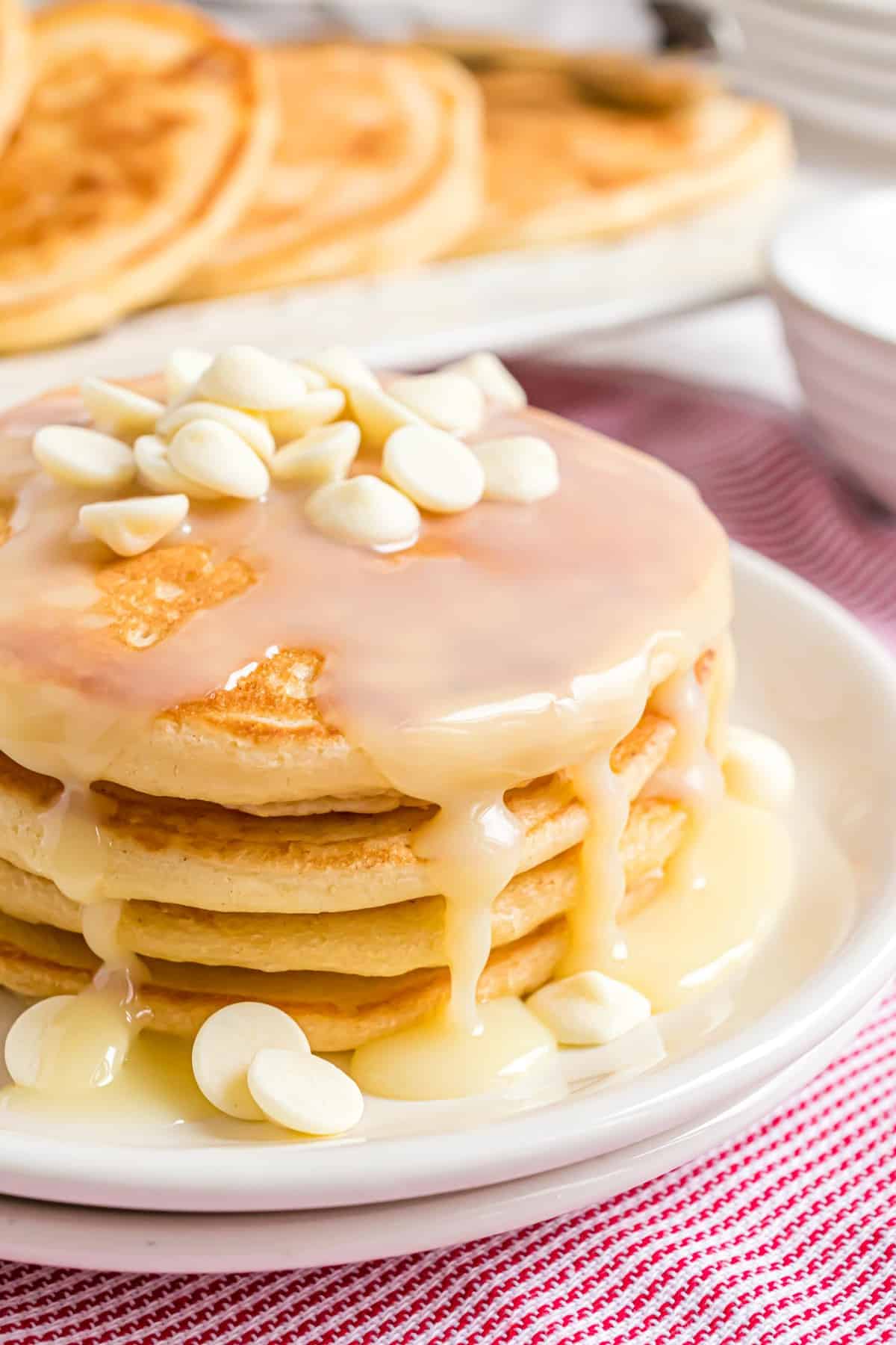 Stack of white chocolate pancakes with syrup and white chocolate chips.