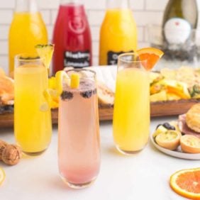 Three different varieties of mimosas with brunch foods in background.
