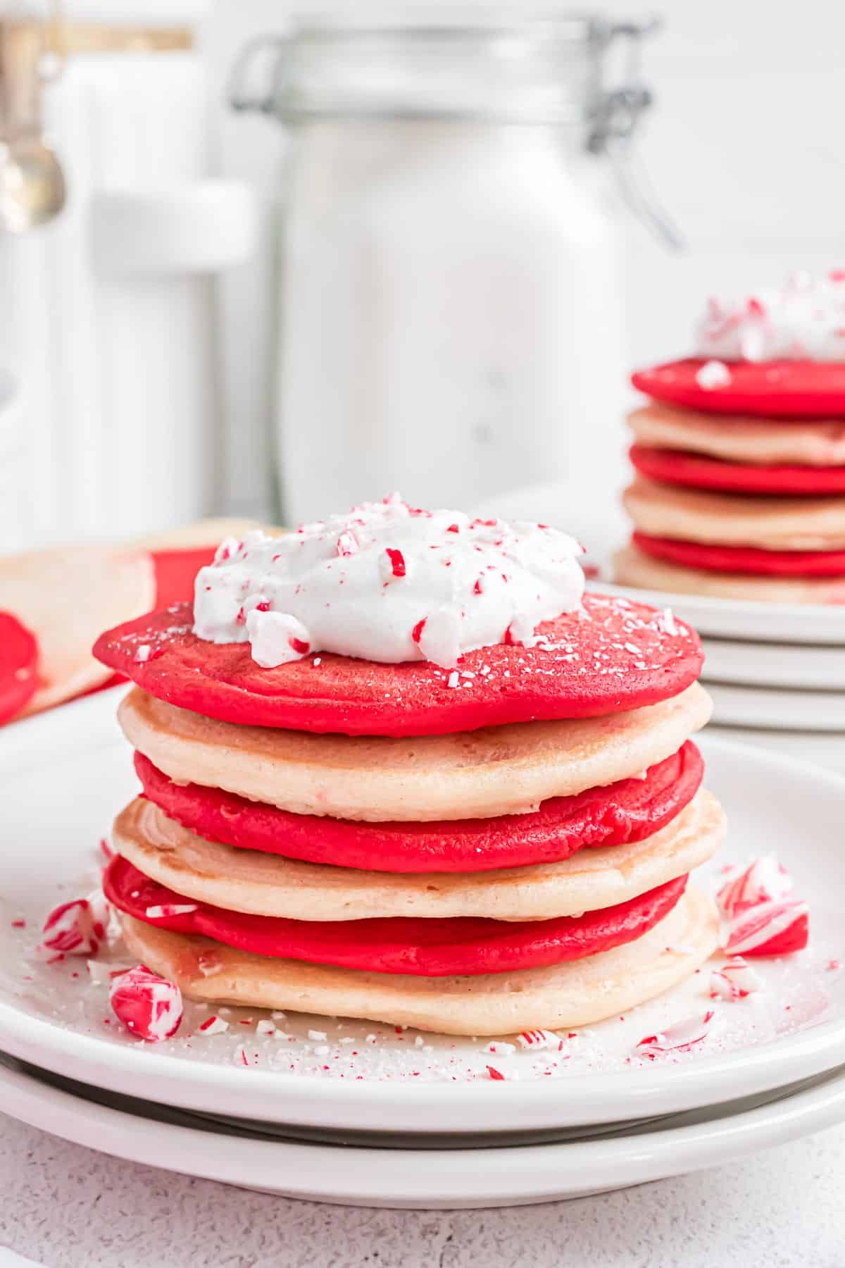 Stack of red and white pancakes topped with whipped cream and crushed candy cane.