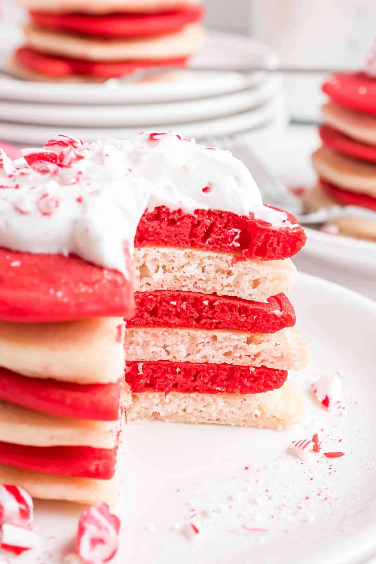 Stacked red and white candy cane pancakes with whipped cream.