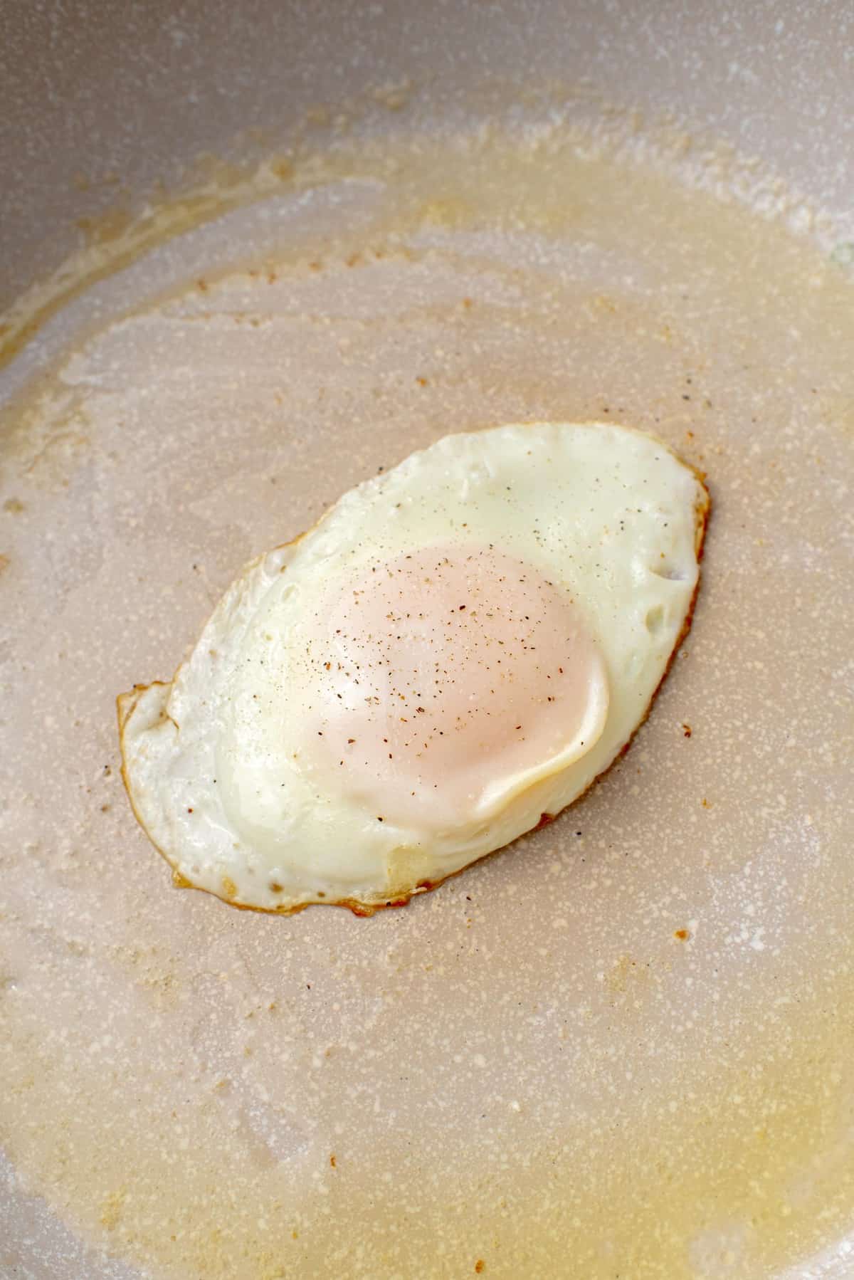 Egg in a pan, with butter pooled on one side of pan.
