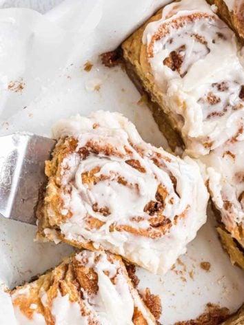 Crescent roll cinnamon rolls in a white baking dish, one on a spatula.