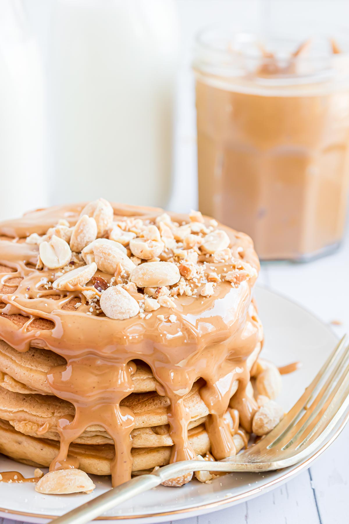Stack of peanut butter pancakes with peanut butter drizzle and peanuts.