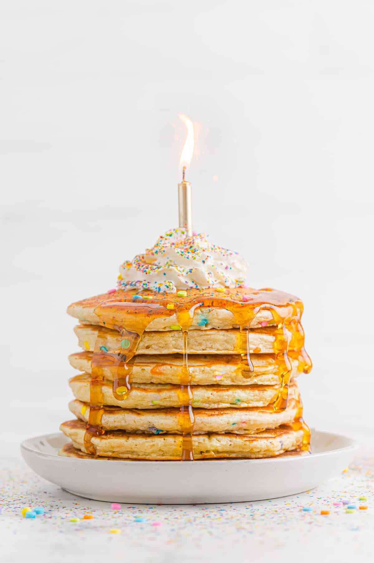 Birthday cake pancakes with whipped cream, sprinkles, and a candle.