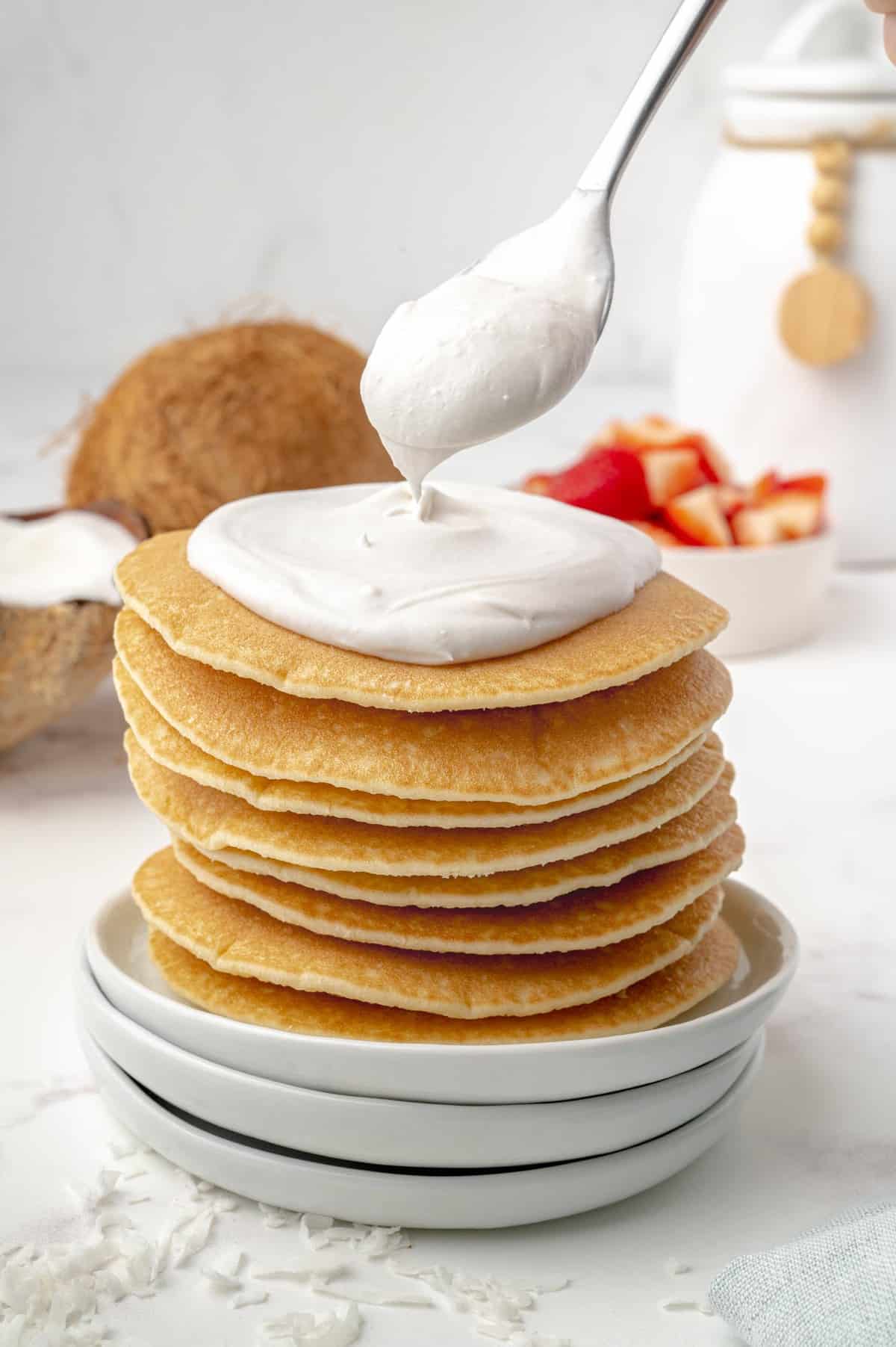 Pancakes being topped with coconut whipped cream topping.
