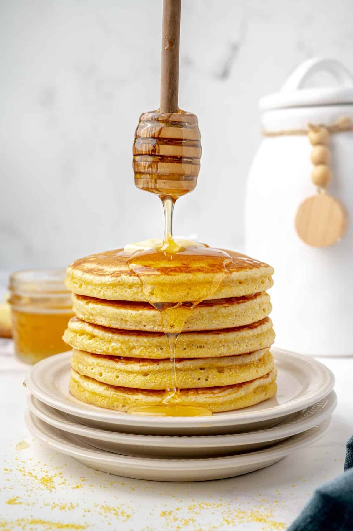 Stack of cornbread pancakes with honey being drizzled on them.