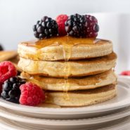 Stack of fluffy pancakes topped with berries and syrup.