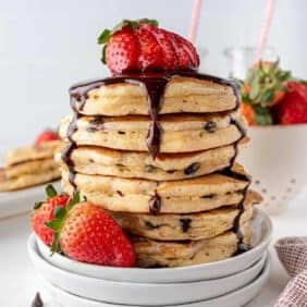Stack of strawberry chocolate chip pancakes with chocolate syrup.