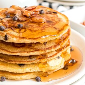 Stack of bacon and chocolate chip pancakes with syrup.