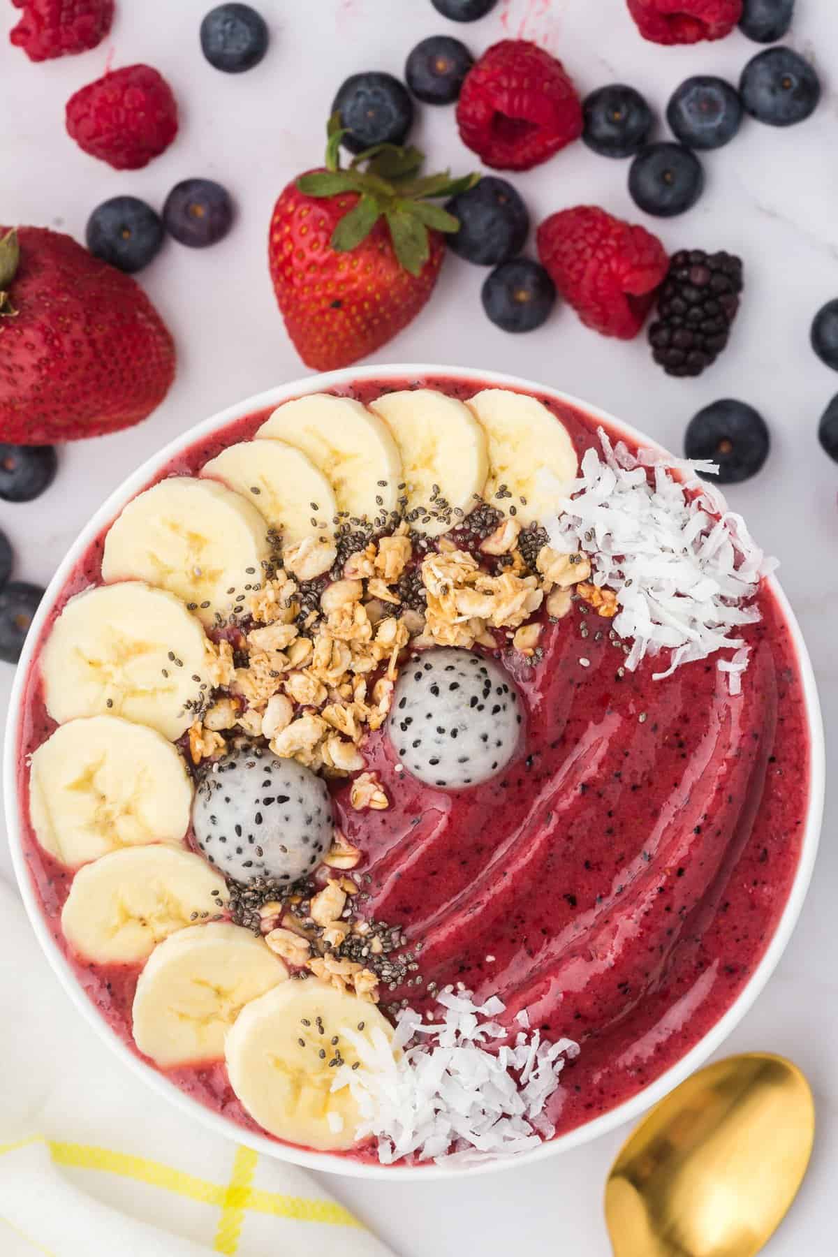 Berry smoothie bowl topped with bananas, granola, coconut.