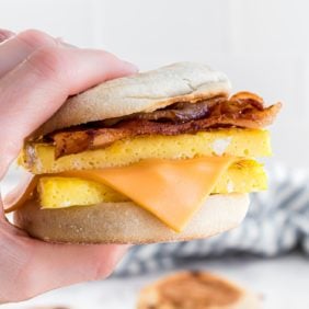 Egg breakfast sandwich with bacon being held in someone's hand.