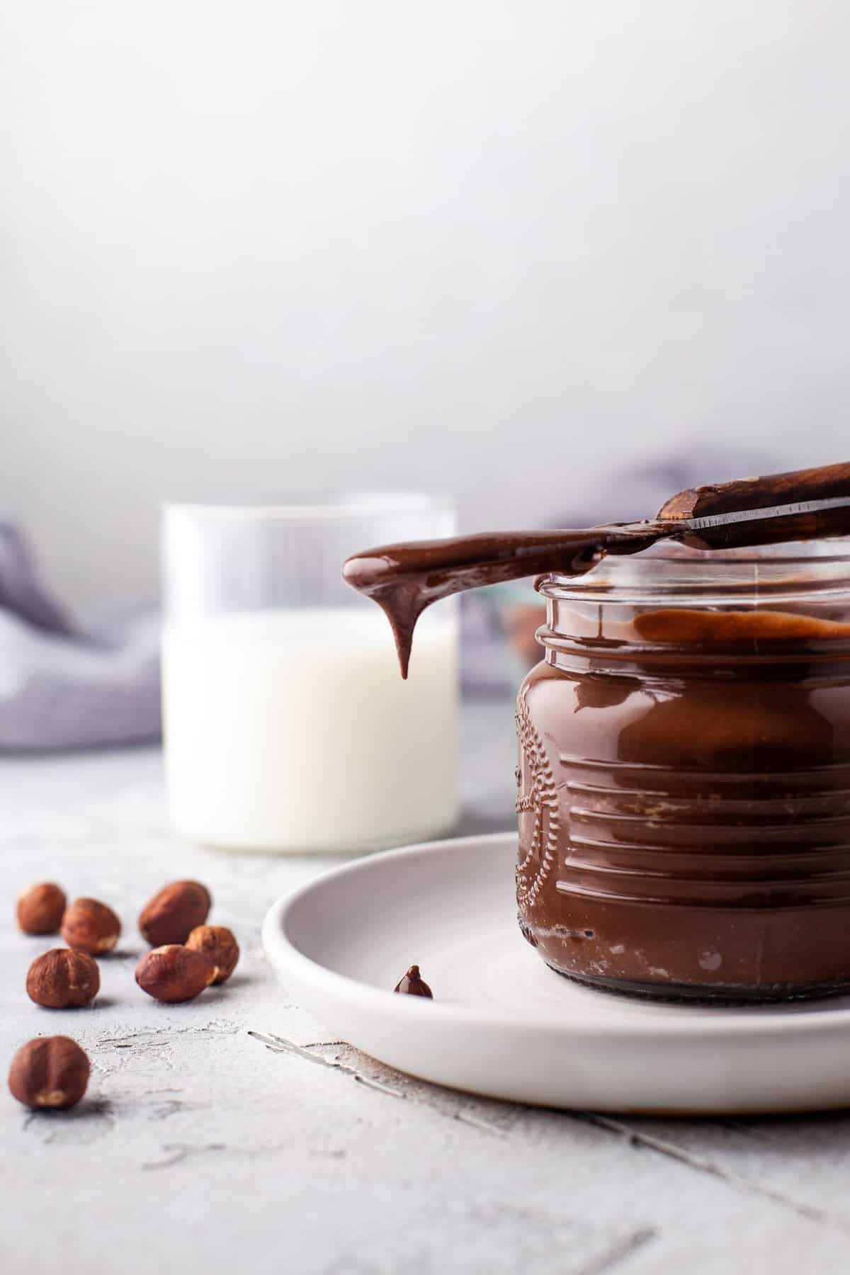 Nutella dripping off a knife set atop a jar.