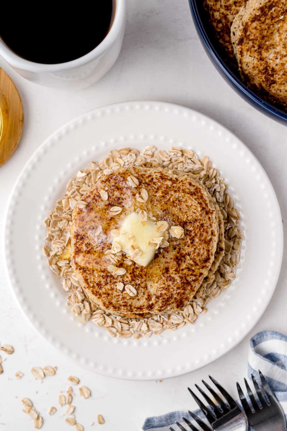 Overhead view of a stack of pancakes with butter, honey, and oats.