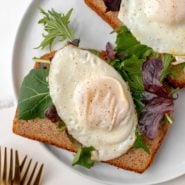 Basted egg on top of toast with greens on white plate.