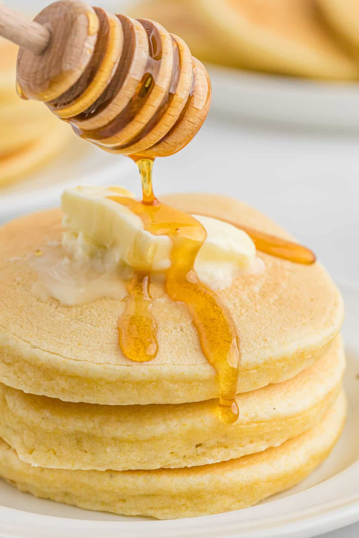 Syrup being drizzled on cornmeal pancakes with butter.