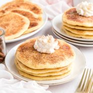 Three plates of snickerdoodle pancakes, topped with whipped cream.