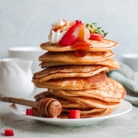 Tall stack of strawberry ricotta pancakes with strawberries on top.