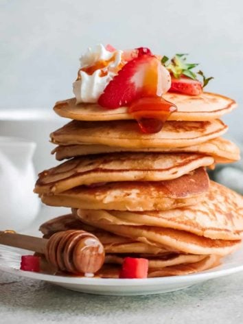Tall stack of strawberry ricotta pancakes with strawberries on top.