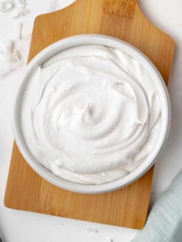Coconut whipped cream in a white bowl on a wood cutting board.