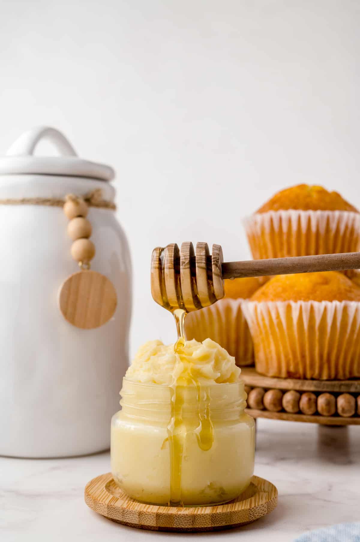 Honey butter in a small jar with corn muffins in the background.