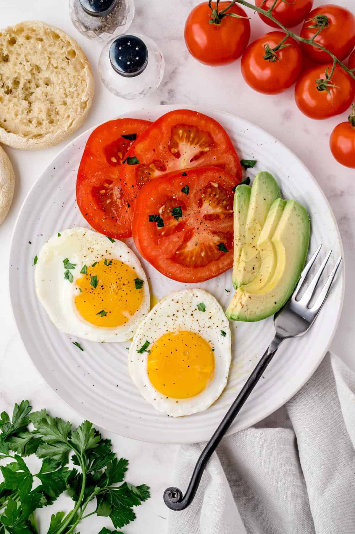 Plate of breakfast food including sunny-side up eggs, tomatoes, avocado.