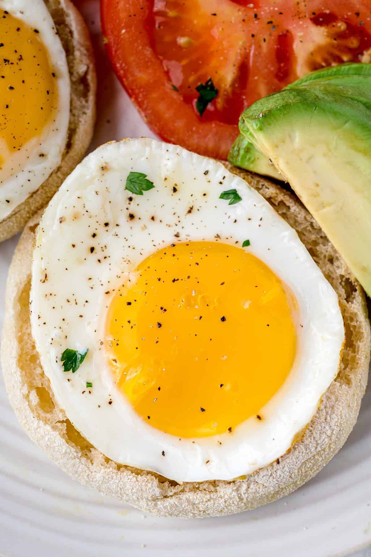 Sunny side up egg on a plate with avocado and tomato.