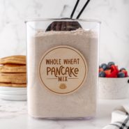 Labeled canister with whole wheat pancake mix and a scoop.