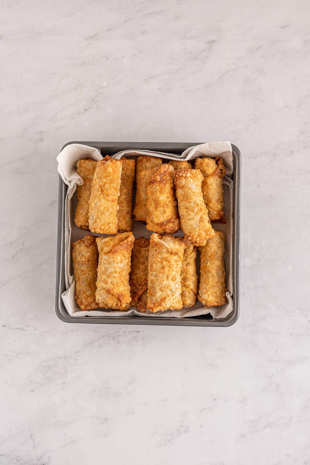 Cooked egg rolls in small square pan.