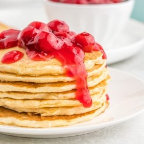 Cherry pie pancakes stacked with cherries on top.