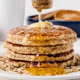 Stack of honey oat pancakes being drizzled with honey.