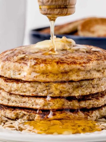 Stack of honey oat pancakes being drizzled with honey.