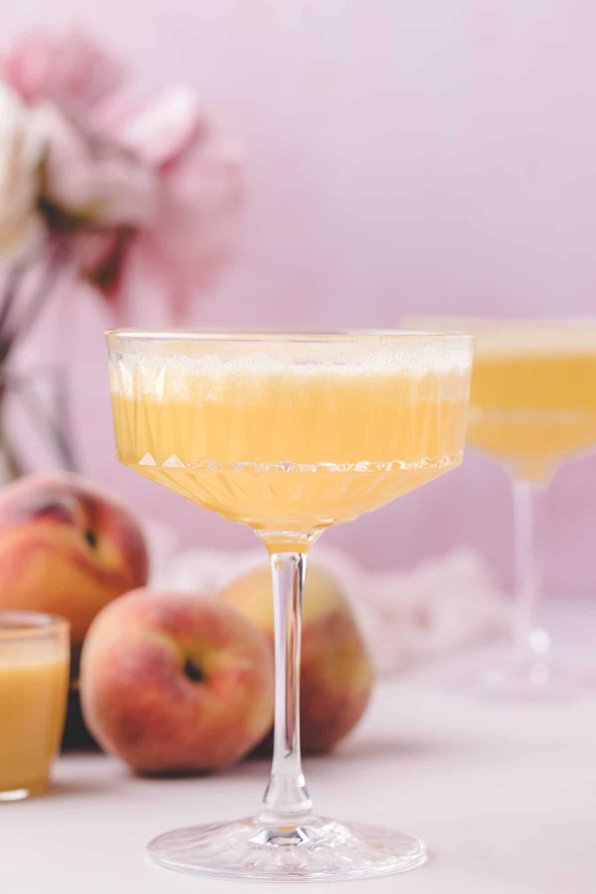 Peach Bellini cocktail against a pinkish purple background.