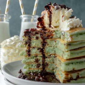 Stack of mint chocolate chip pancakes with whipped cream and chocolate sauce.