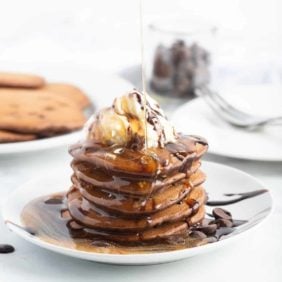 Syrup being poured on a stack of chocolate pancakes.