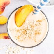 Overhead view of a peach smoothie garnished with fresh peach and oats.