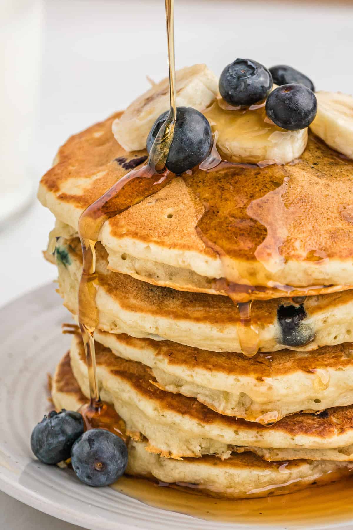 Banana blueberry pancakes being drizzled with syrup.